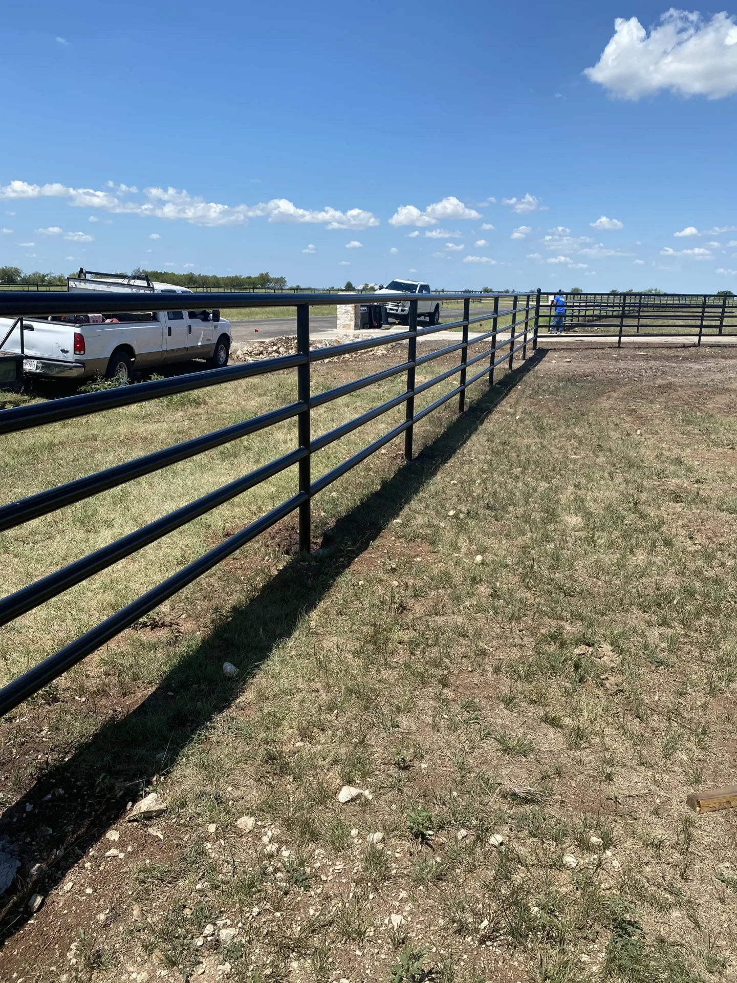Truck parked in a field next to a black metal fence, with a person standing nearby